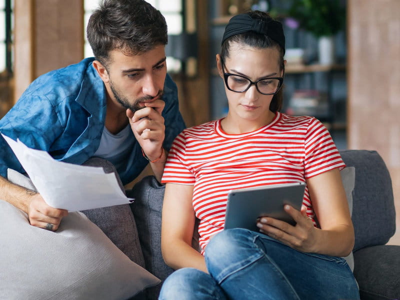 Couple assis sur un canapé tient des documents et utilise une tablette