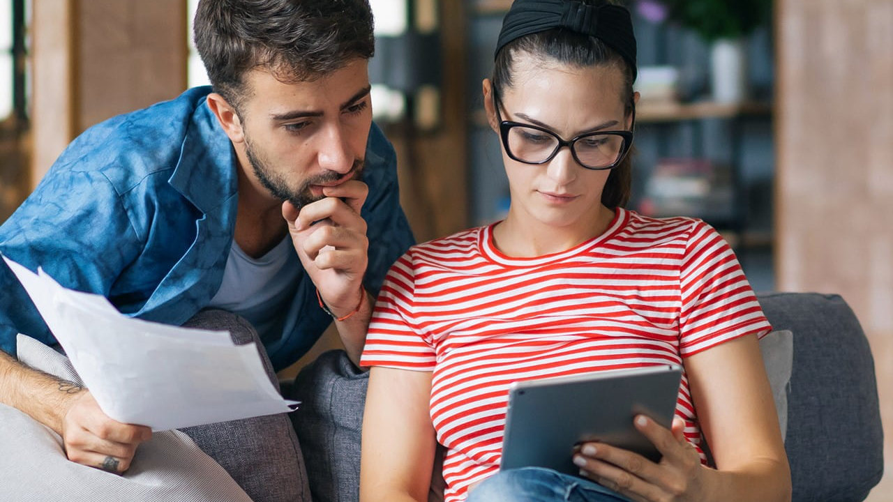 Couple assis sur un canapé tient des documents et utilise une tablette