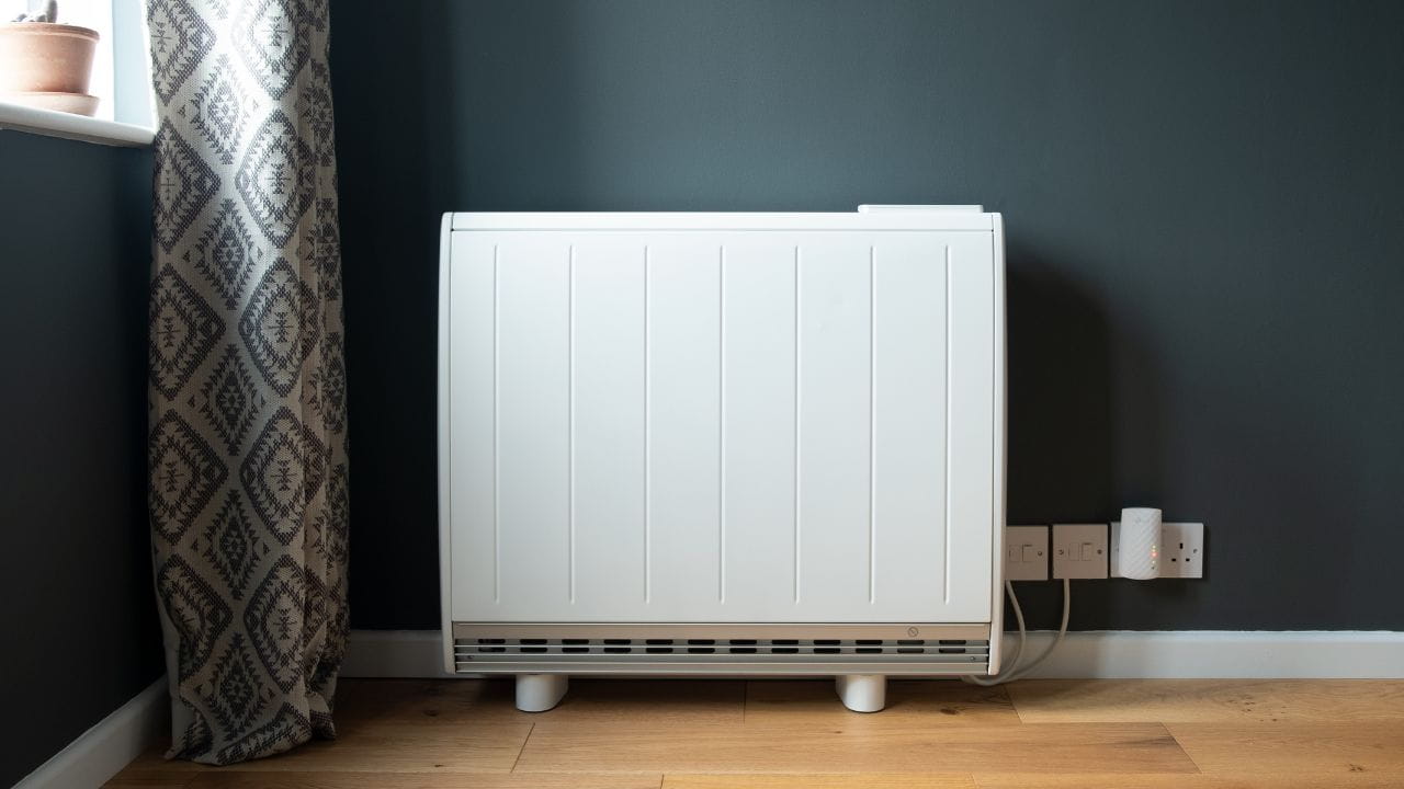 Radiateur électrique blanc contre un mur foncé, à côté d’une fenêtre, dans une pièce.
