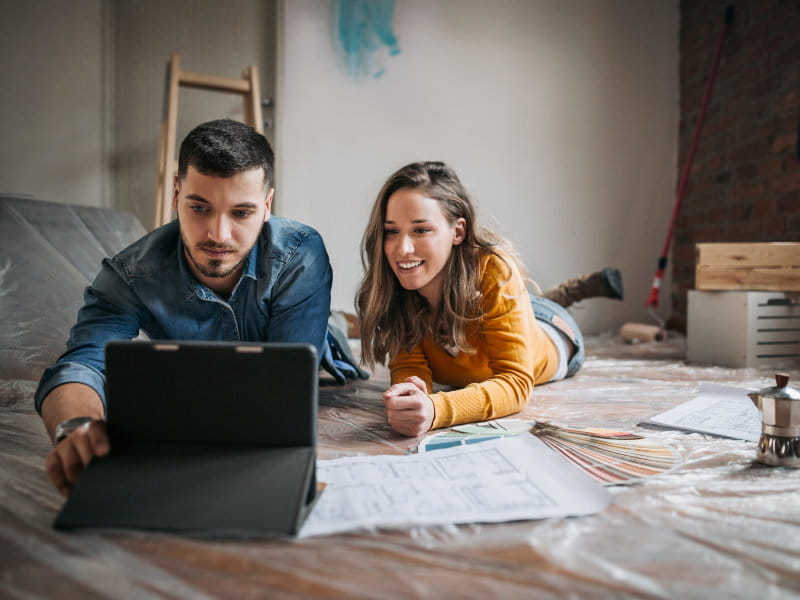 Couple est allongé au sol, regarde une tablette et examine des plans et échantillons de couleurs