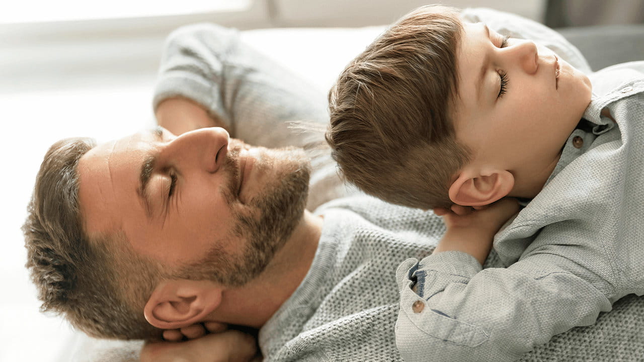 Homme est allongé sur le dos, enfant allongé sur lui, tous deux ont les yeux fermés