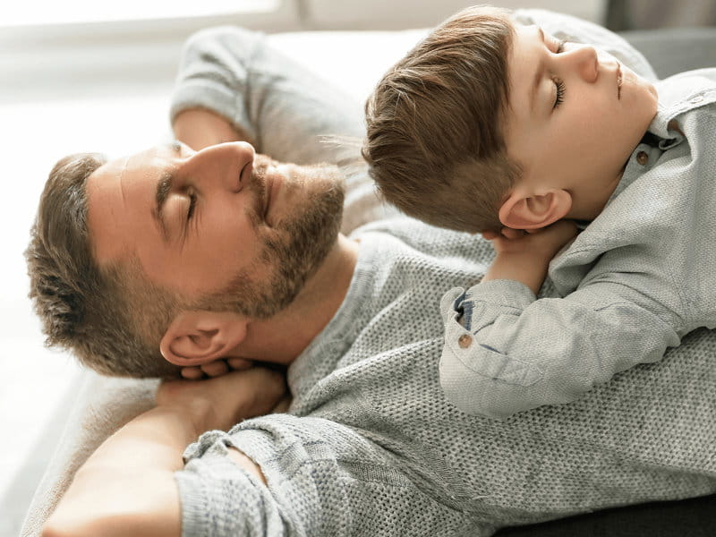 Homme est allongé sur le dos, enfant allongé sur lui, tous deux ont les yeux fermés