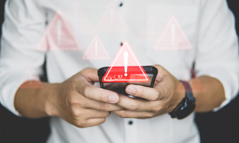 Personne tient un smartphone, des symboles d’avertissement avec point d’exclamation apparaissent au-dessus