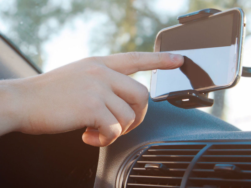 Main utilise un smartphone fixé dans une voiture pour la navigation ou la recherche d’emplacement