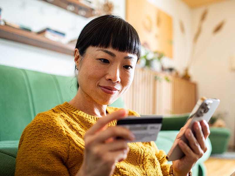 Femme tient un smartphone et une carte bancaire pour effectuer un paiement numérique