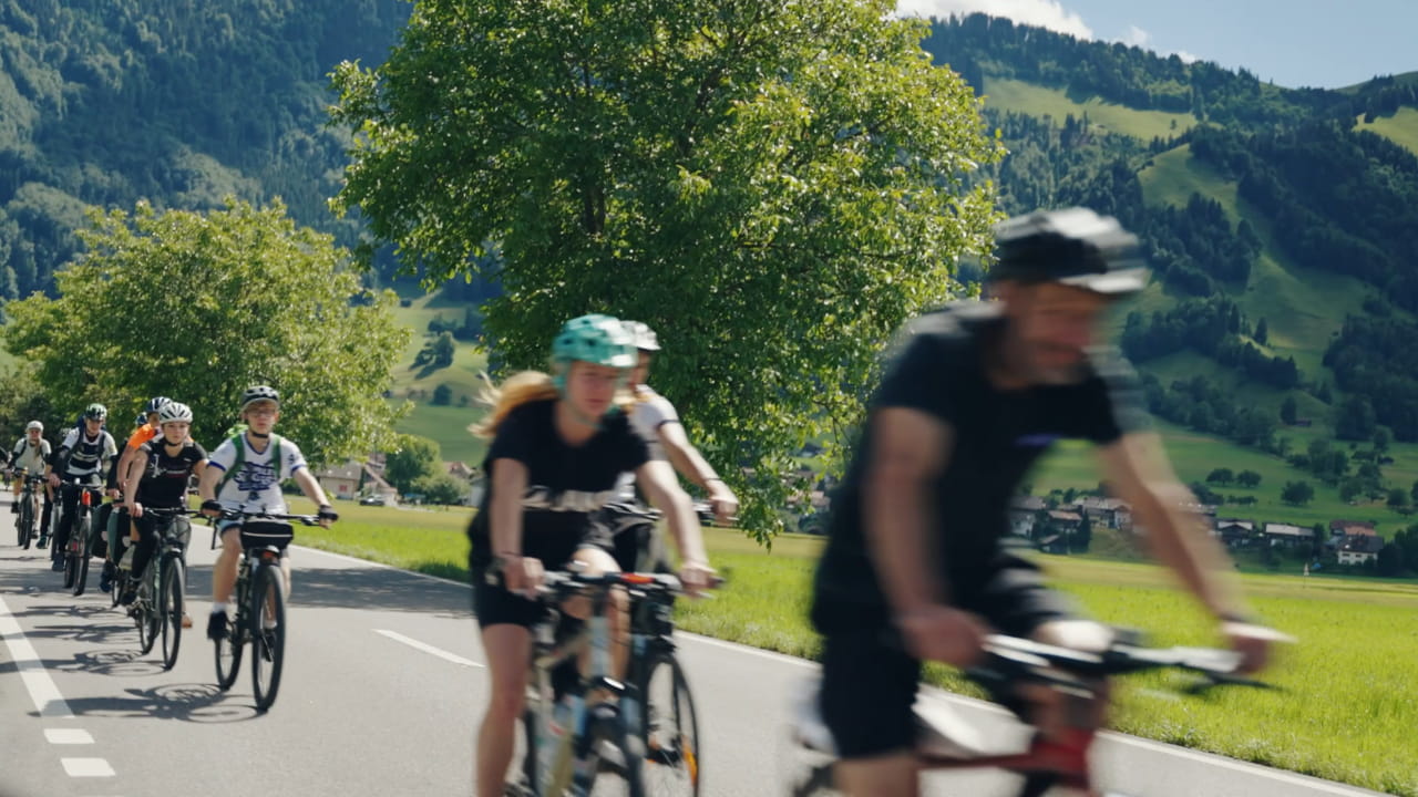 Un groupe en camp scolaire roule à vélo sur une route de campagne dans un paysage de collines verdoyantes.