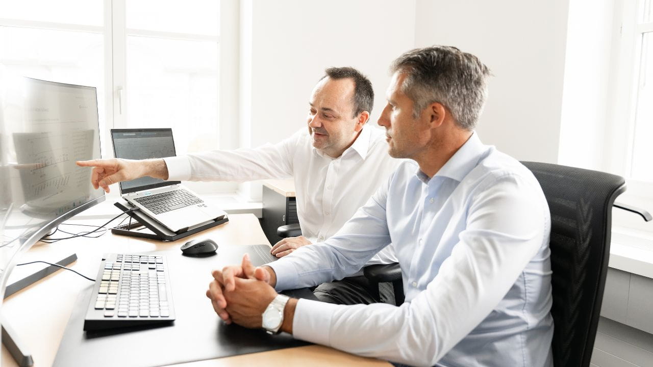 Deux hommes consultent ensemble des graphiques sur un écran à leur poste de travail.
