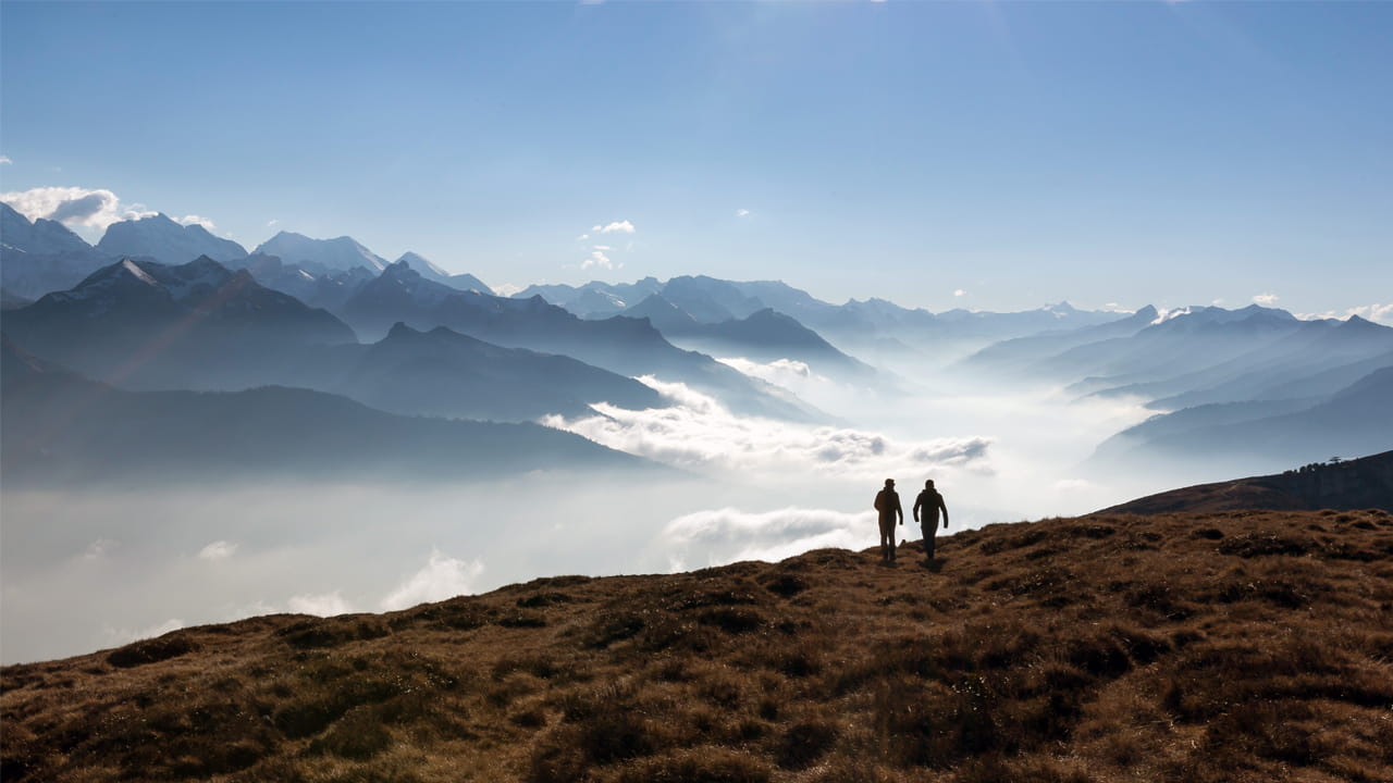 Deux personnes marchent sur une crête de montagne avec vue sur une mer de nuages et les Alpes