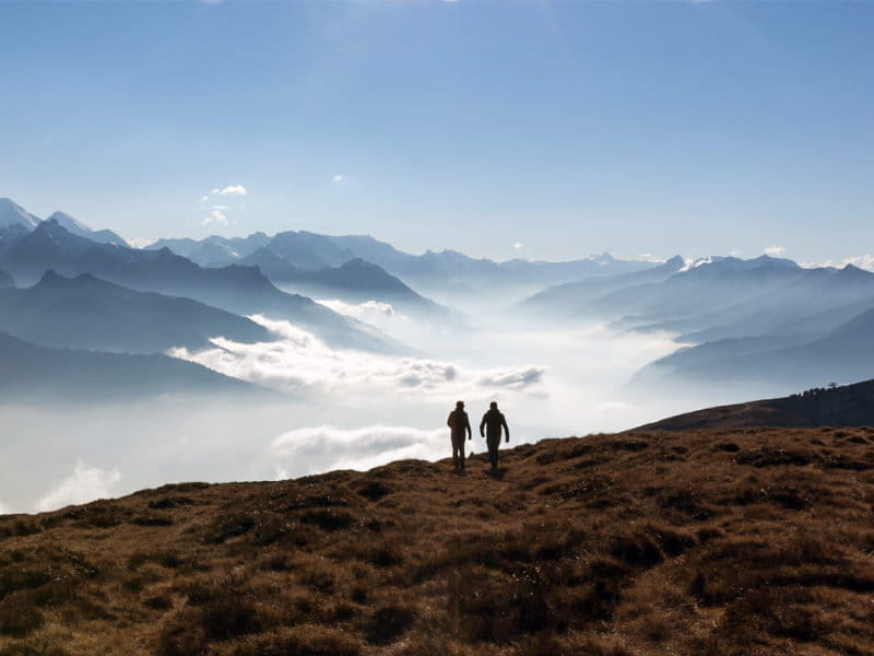 Deux personnes marchent sur une crête de montagne avec vue sur une mer de nuages et les Alpes