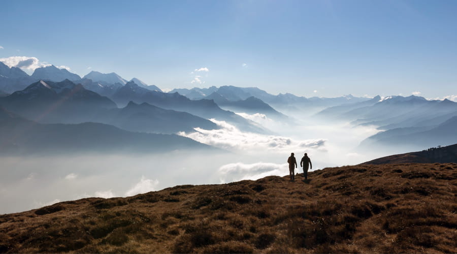 Deux personnes marchent sur une crête de montagne avec vue sur une mer de nuages et les Alpes