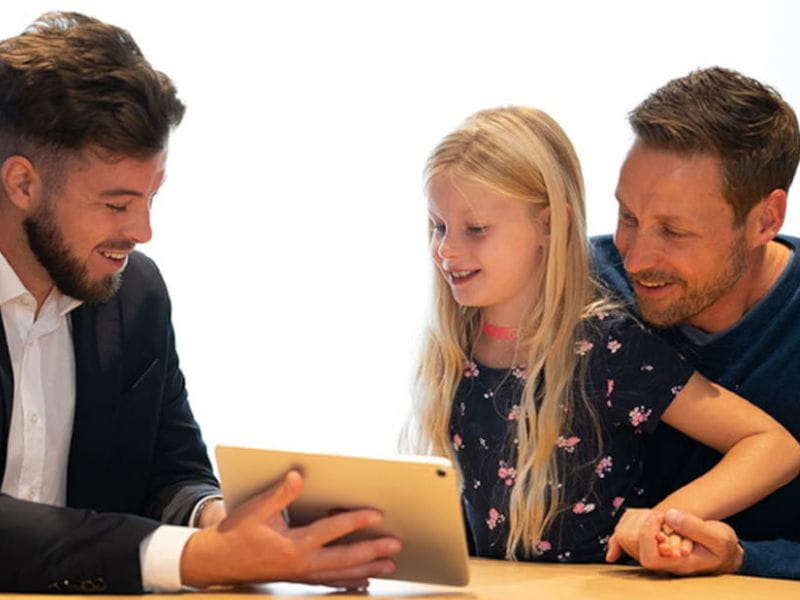 Un conseiller montre quelque chose sur une tablette à un père et à sa fille.