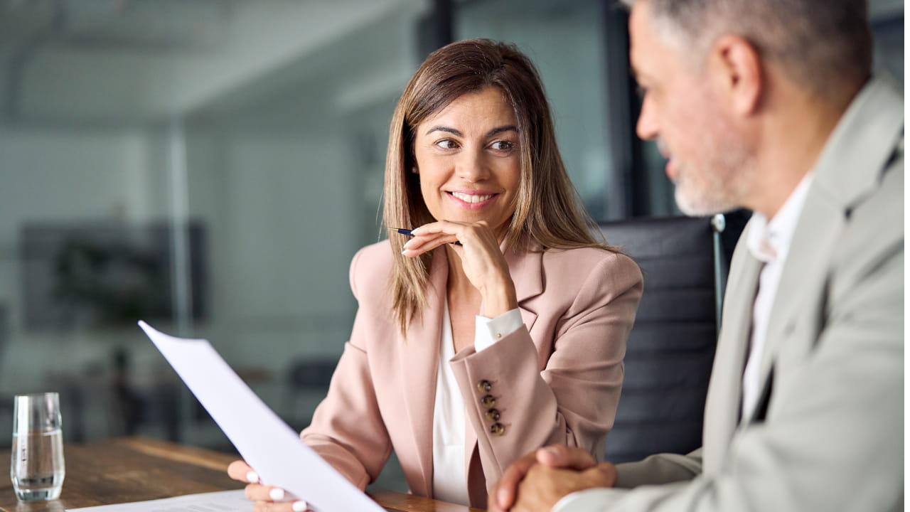 Une femme et un homme discutent ensemble d’un document autour d’une table de réunion au bureau.