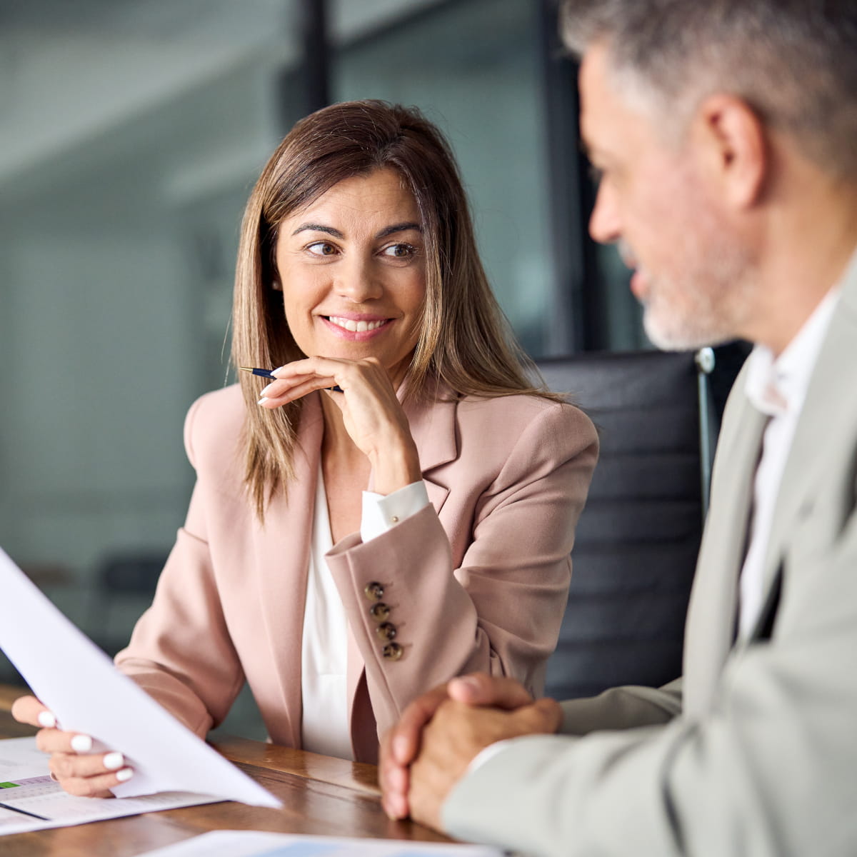 Une femme et un homme discutent ensemble d’un document autour d’une table de réunion au bureau.