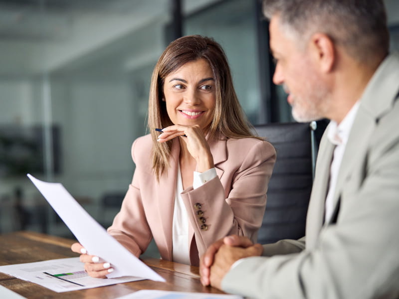 Une femme et un homme discutent ensemble d’un document autour d’une table de réunion au bureau.