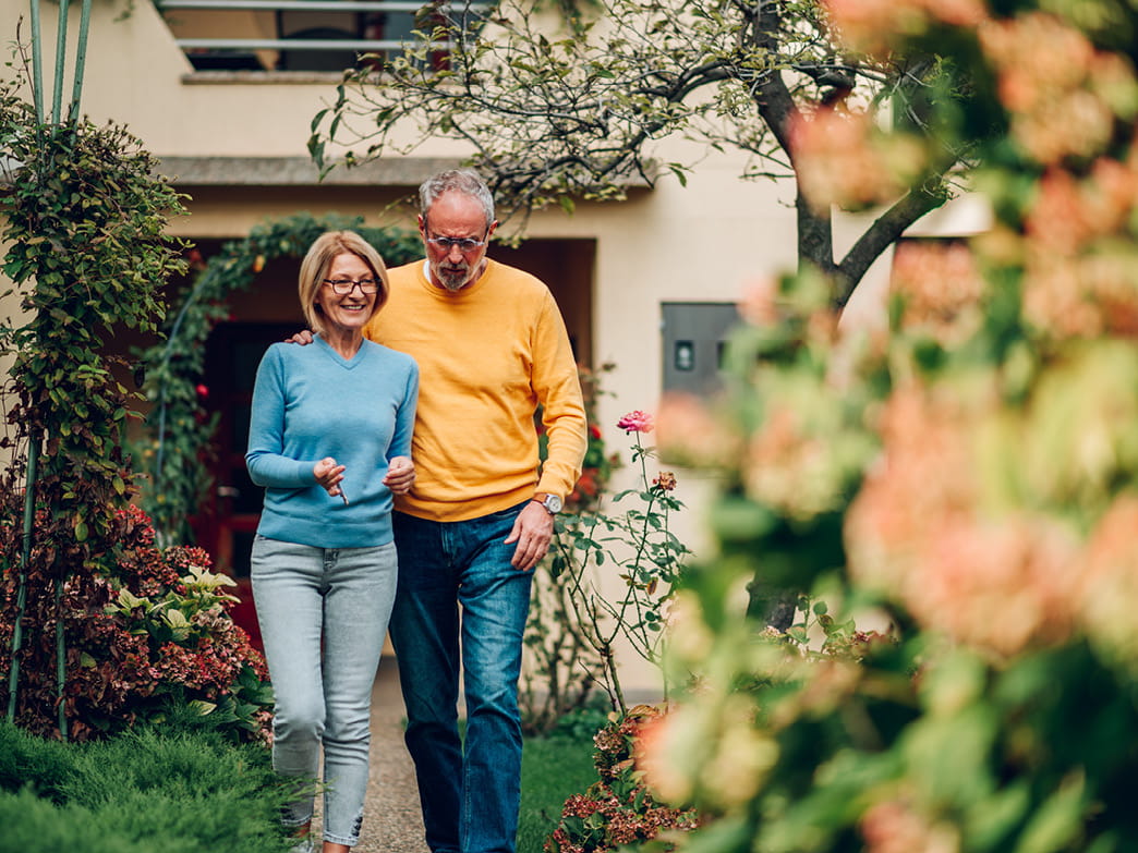 Couple âgé marche ensemble dans un jardin devant la maison