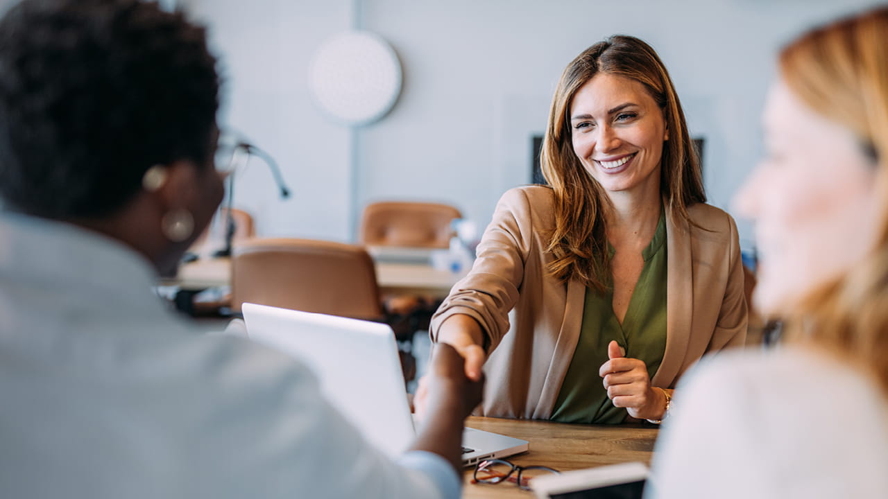 Conseillère à la clientèle serre la main d’une personne lors d’un entretien de conseil à table